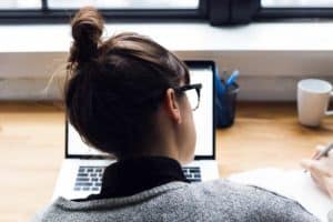 female taking notes and browsing laptop 4460x4460